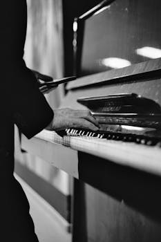 Monochrome close-up of hands playing a piano in a vertical shot.