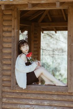 Elegant Asian woman in a window frame holding a rose, eyes closed in serenity.