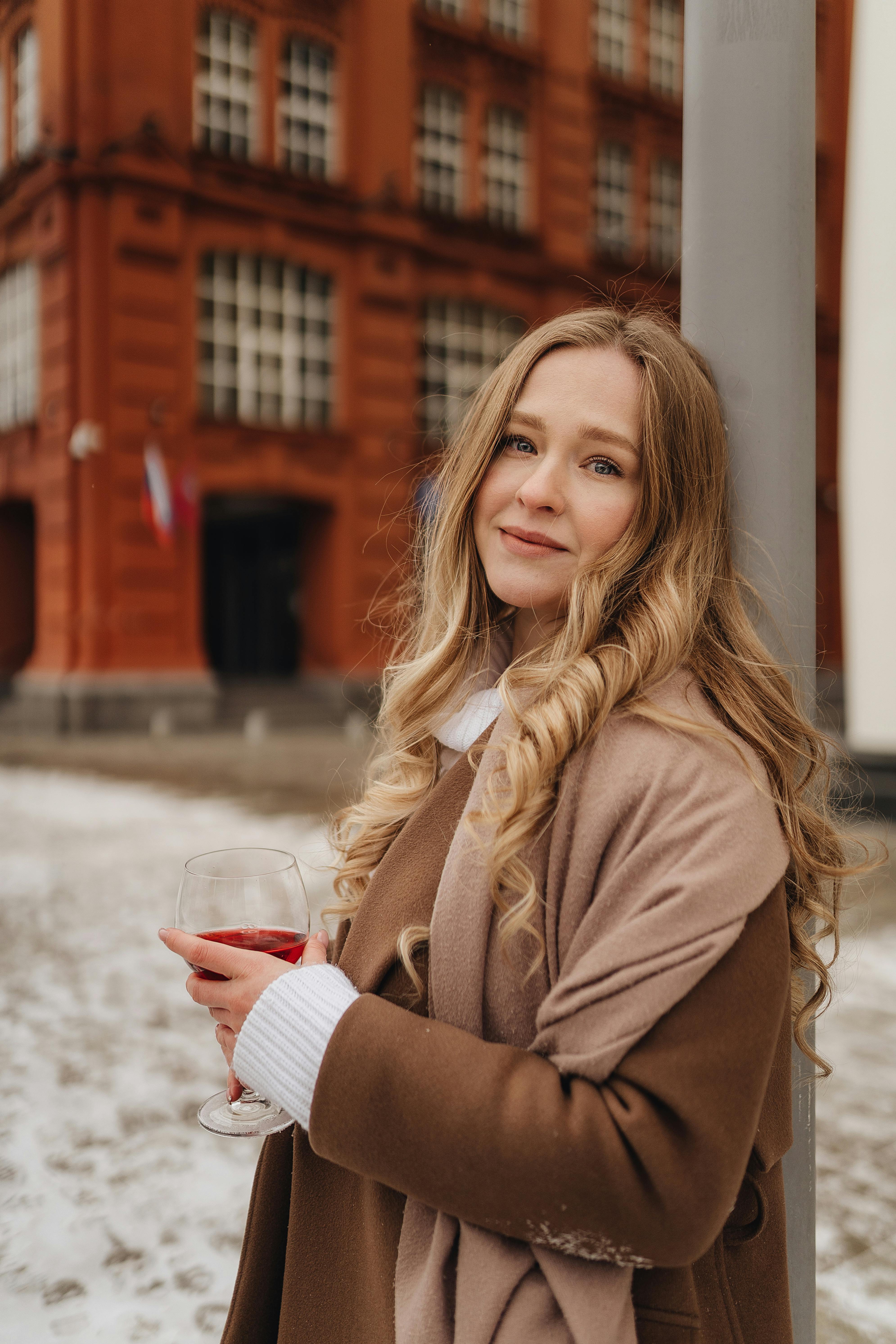 woman with glass of red wine in hand leaning against street pole