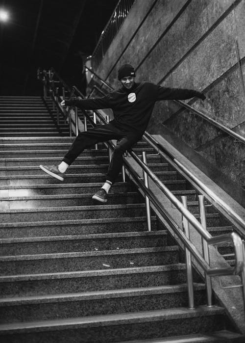 Grayscale Photo of Man Sliding on Handrail