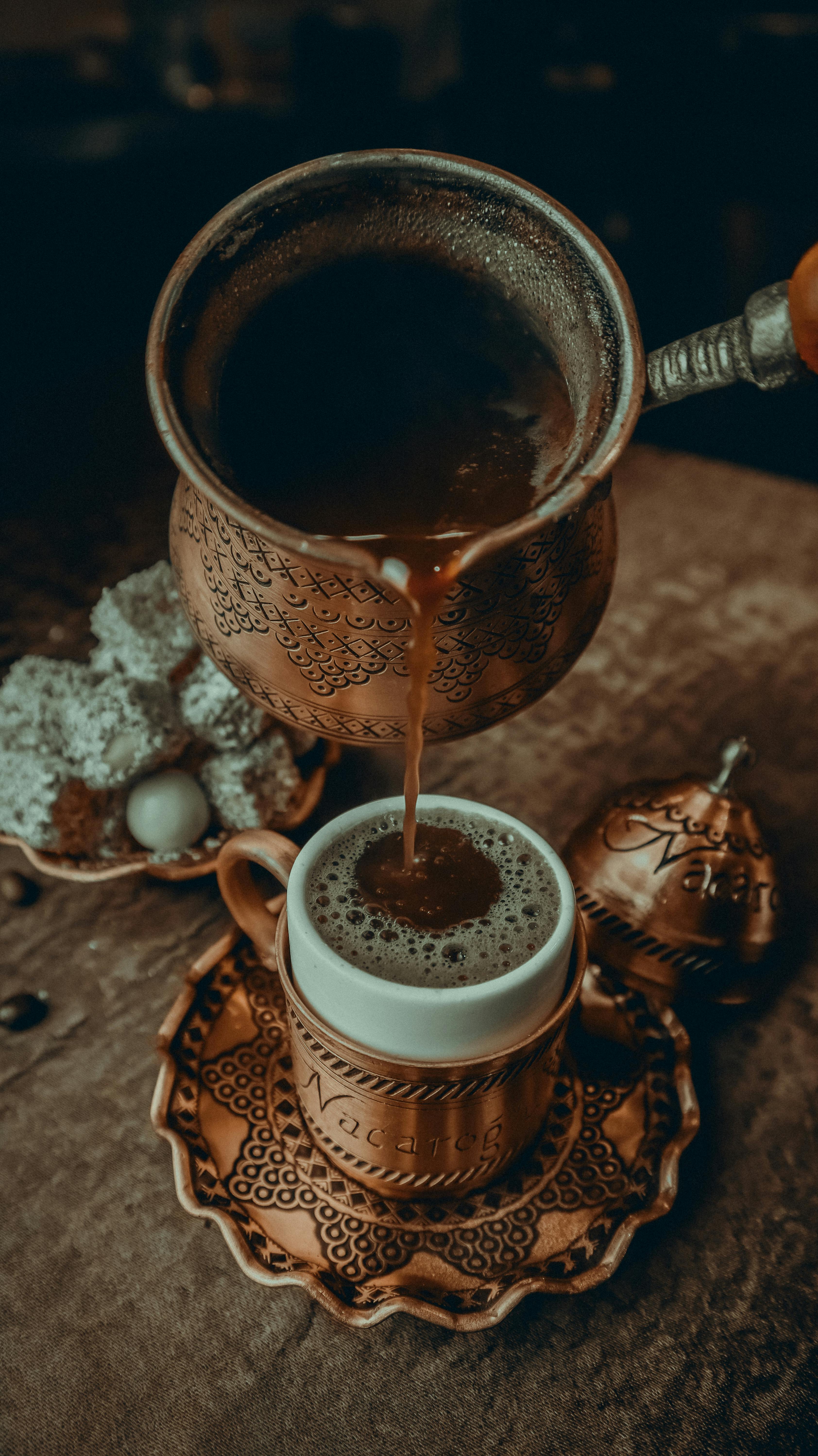 unrecognizable hand pouring coffee from turkish ornate copper skillet to cup