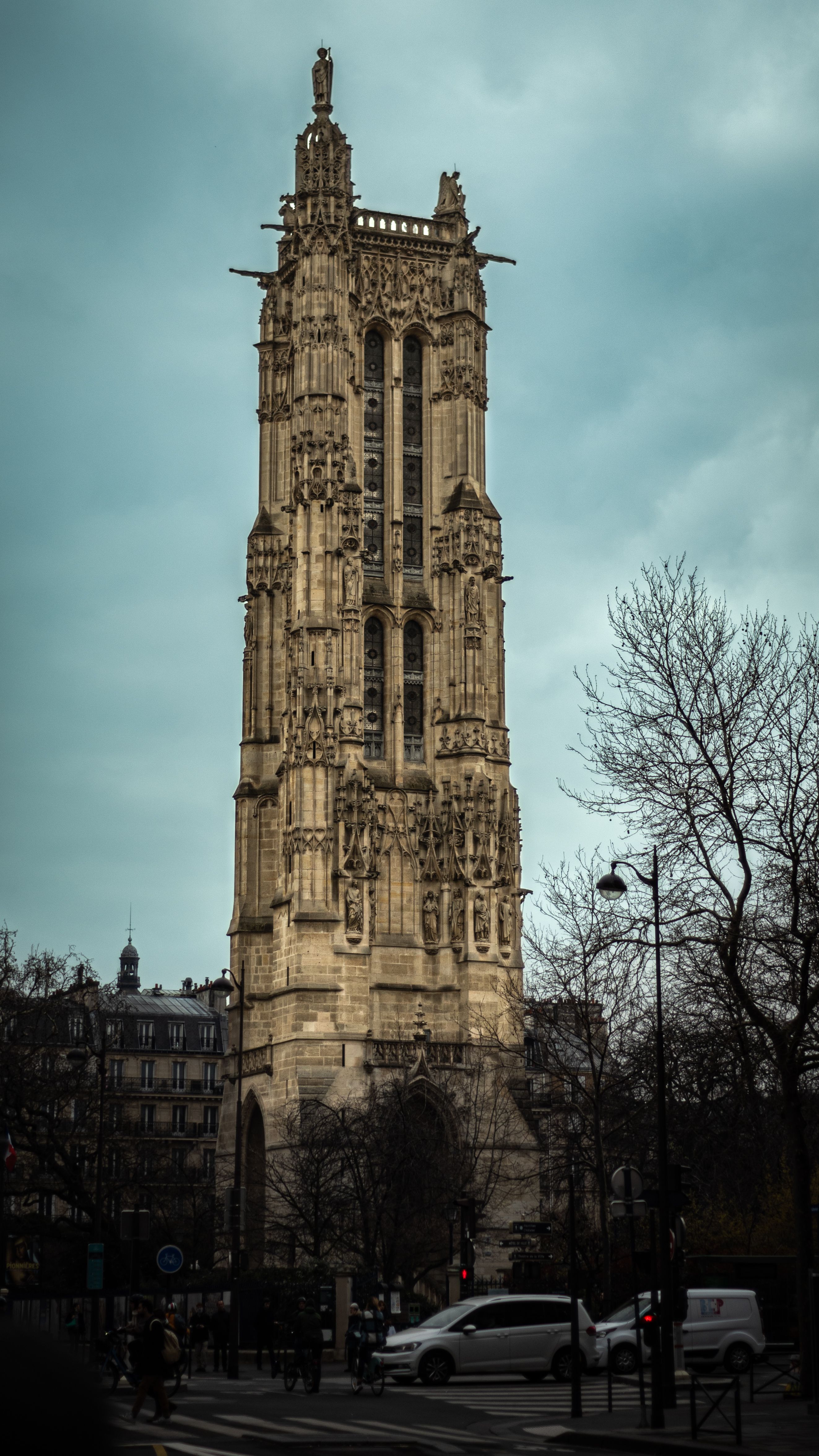 Gothic Saint-Jacques Tower in Paris under a gloomy sky with leafless trees and street view.