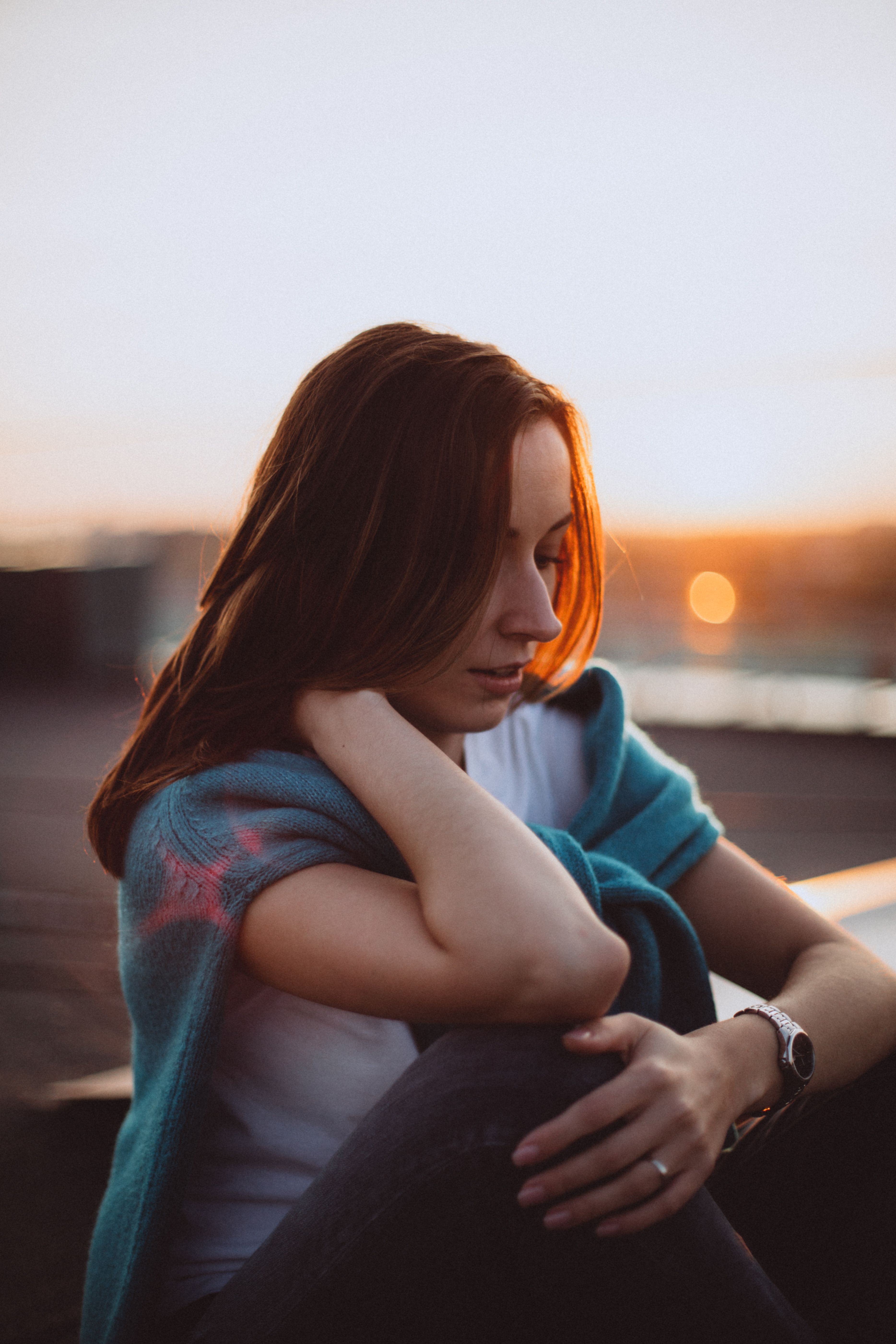 Woman sitting outdoors, wrapped in a teal shawl, at sunset, looking contemplative.