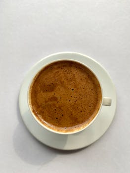 A close-up overhead shot of a steaming cup of frothy coffee in a white cup and saucer.