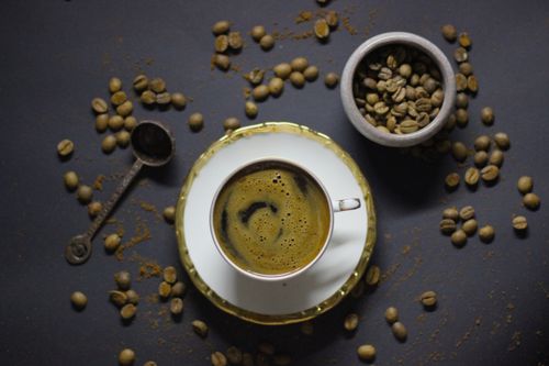 Free Elegant flatlay composition featuring a cup of coffee with froth, surrounded by scattered coffee beans and a scooper. Stock Photo