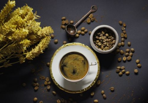 Free A vibrant flat lay of a coffee cup with beans and flowers on a dark surface. Stock Photo