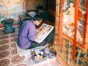 Artisan carefully painting a Buddhist thangka in an indoor workshop, showcasing intricate artistry and cultural heritage.