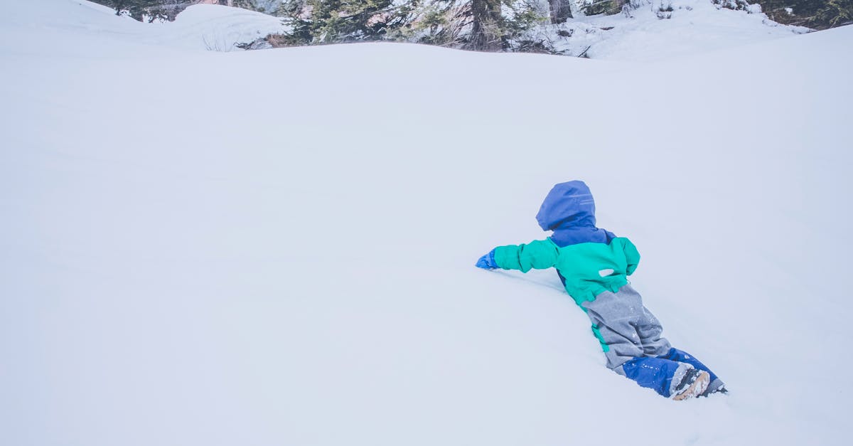 Toddler in Blue and Green Snow Suit on Snow Field during Daytime