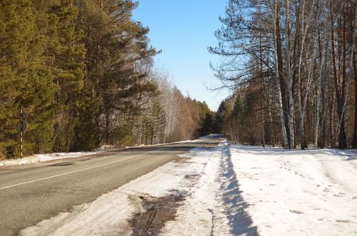 Free A picturesque winter scene with a road cutting through lush forests under a clear blue sky. Stock Photo