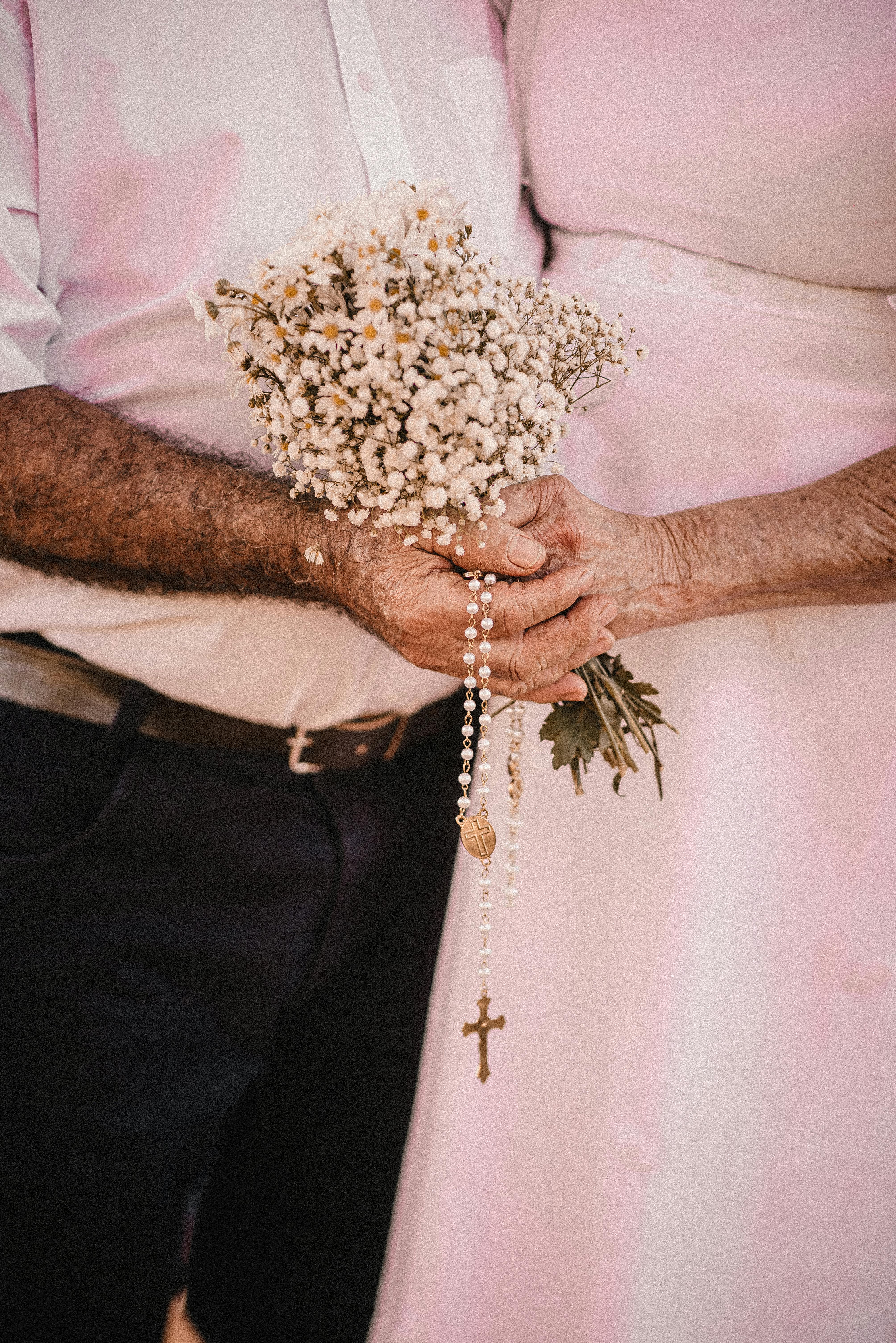 Elderly couple holding a bouquet and rosary, symbolizing love and faith.