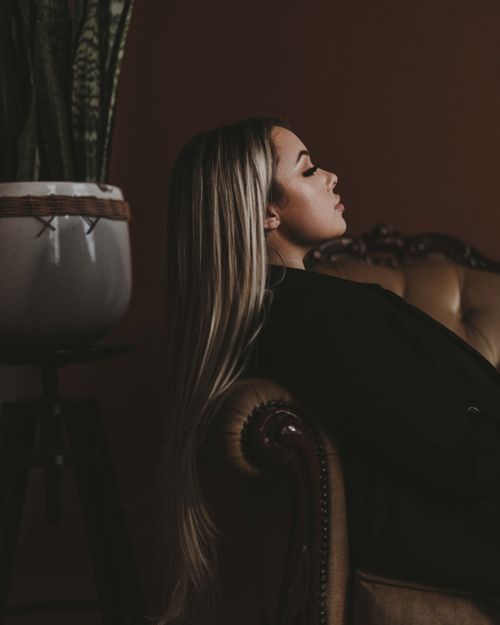 Free Side view of a woman with long hair lying on a sofa beside a potted plant. Stock Photo