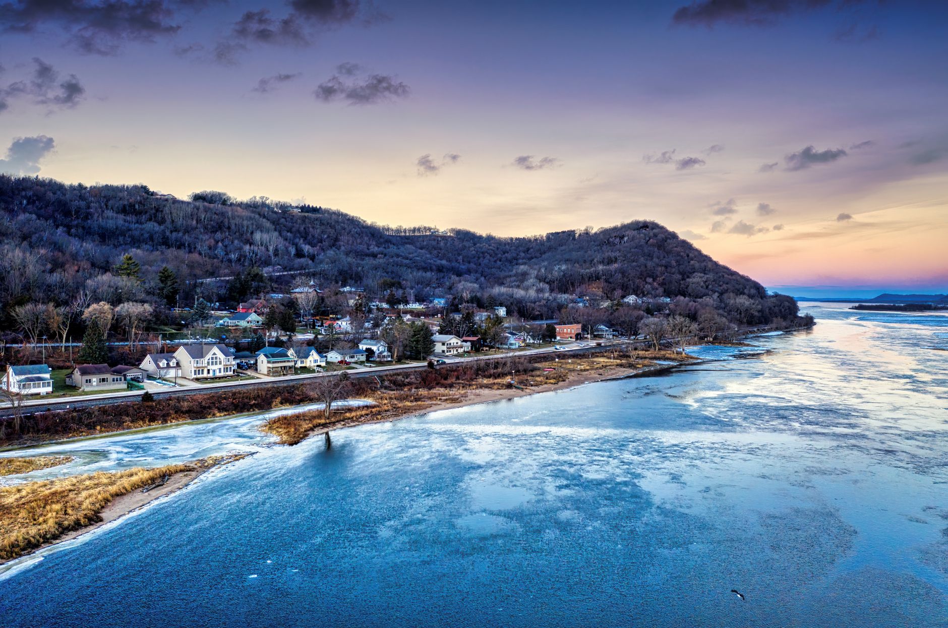 A serene winter sunrise over Reads Landing, Minnesota, showcasing frozen waters and hilly landscapes.