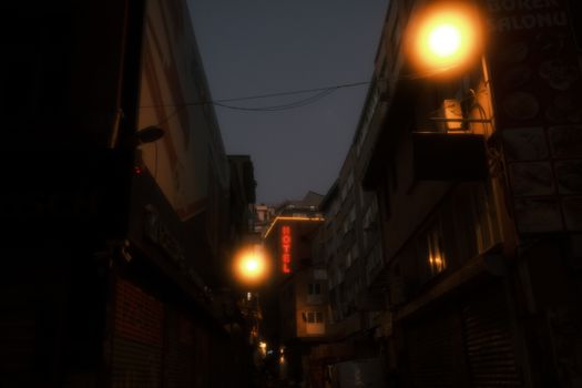 A dimly lit urban alleyway with glowing streetlights and a hotel sign at night.