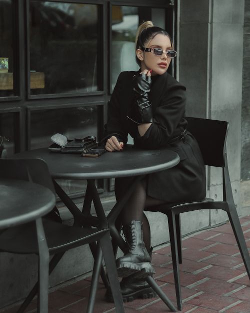 Free Stylish woman in black dress and sunglasses sitting at an outdoor cafe table. Stock Photo