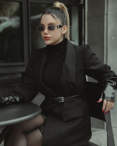 Free Stylish woman in a black outfit and sunglasses sitting outdoors. Stock Photo