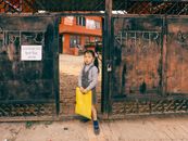 A schoolgirl in uniform holds a yellow bag at a school entrance in Nepal.