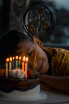 Young boy smiling by a lit birthday cake indoors, creating a warm and happy atmosphere.