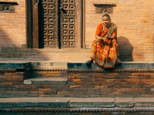Free Indian woman in vibrant dress sitting outside a traditional temple. Stock Photo