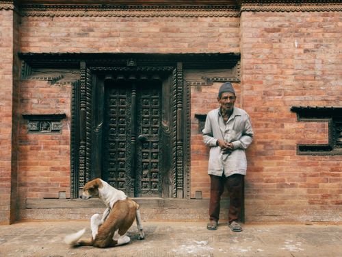 Free Elderly man and dog by ornate doorway of brick building, outdoors. Stock Photo
