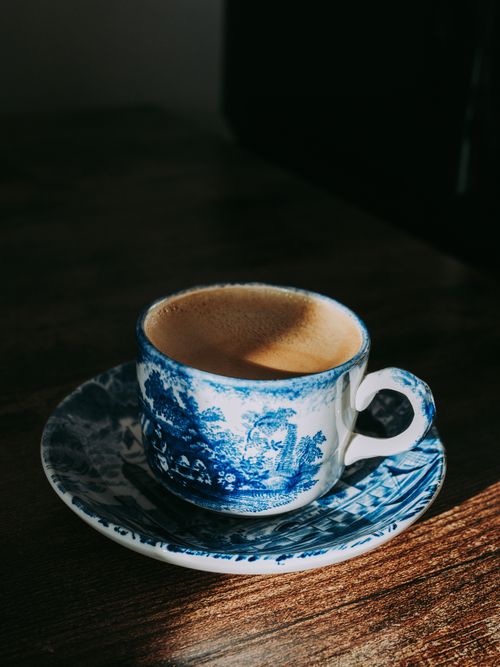 Free Elegant coffee in a blue porcelain cup with saucer, lit by warm sunlight on a wooden table. Stock Photo