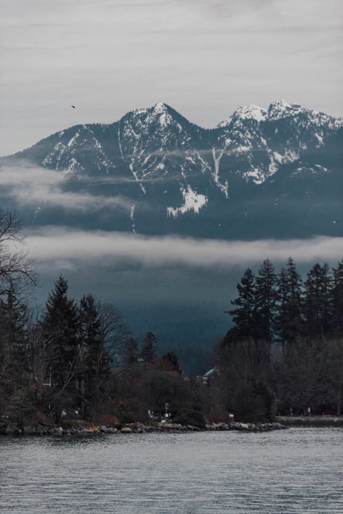 Free Tranquil winter scene with snow-capped mountains and serene lake surrounded by fog and trees. Stock Photo