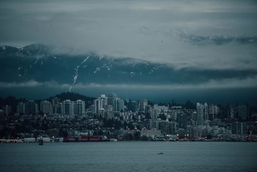 A dramatic view of Vancouver's skyline with fog-covered mountains in the background, evoking a moody ambiance.