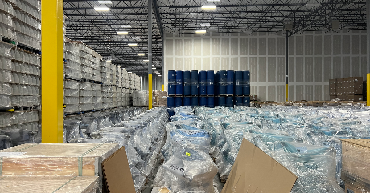 Rows of shrink-wrapped pallets in a distribution warehouse, the safety stock margin PE buyers hold against supplier delays