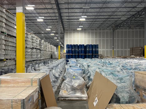Large industrial warehouse filled with stacked goods wrapped in plastic for storage.