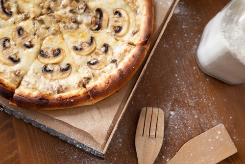 Free Delicious mushroom pizza with cheese in a cardboard box on a wooden table with flour. Stock Photo
