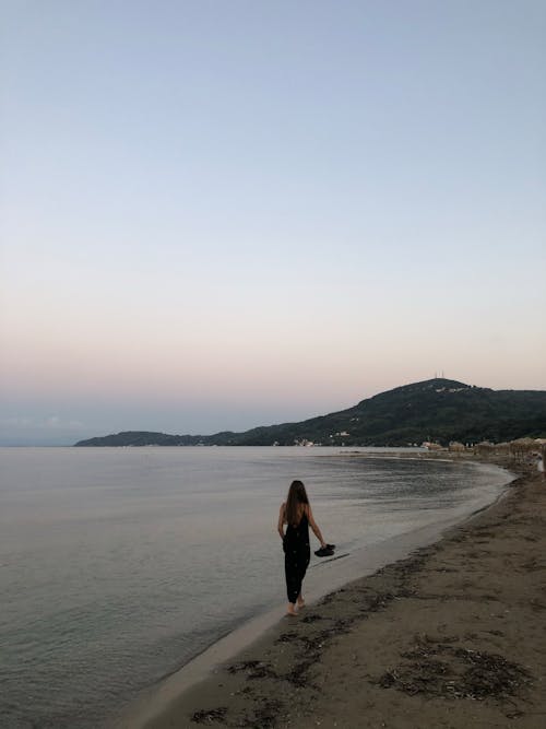 Woman in Black Dress Walking on Seashore