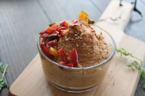 Free Glass bowl of hummus topped with roasted peppers and sesame seeds on a wooden board. Stock Photo