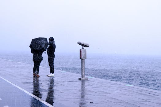 A couple under an umbrella on a rainy day by the Istanbul seashore, with viewing binoculars nearby.