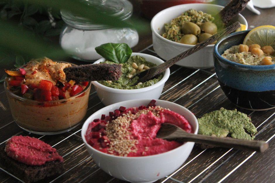 An enticing array of hummus varieties with toppings and colorful garnishes on a wooden table.