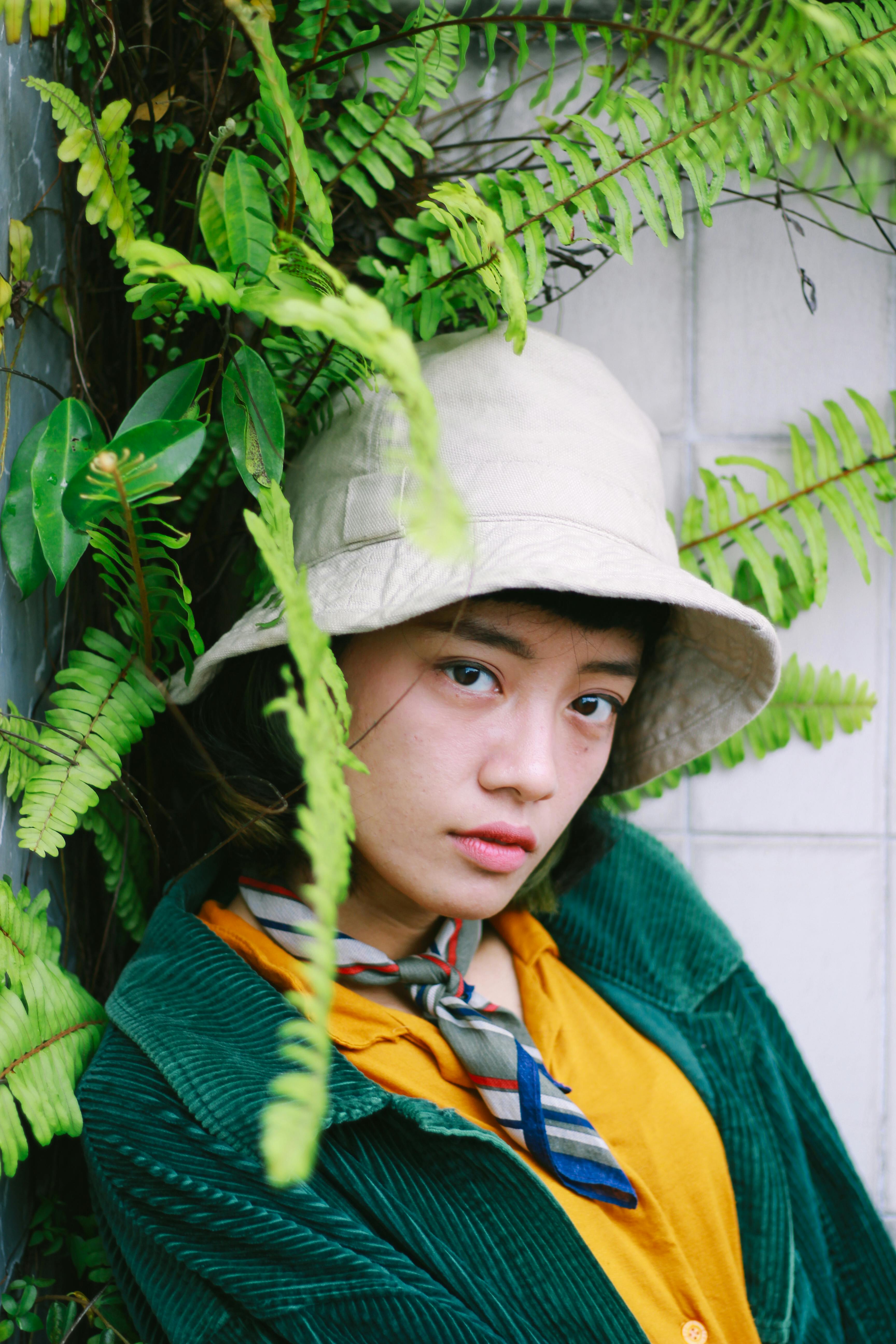 Portrait of a young person with a bucket hat surrounded by lush ferns, exuding a fashionable vibe.