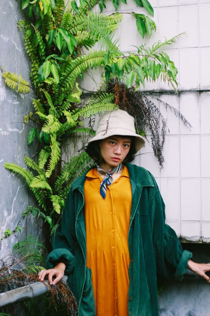 Chic portrait of a woman in a bucket hat against a plant-covered urban wall.