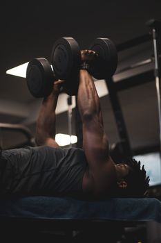 Adult male performing a dumbbell bench press in a gym setting.