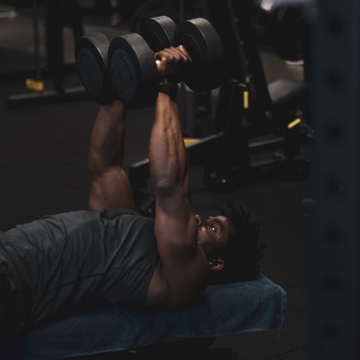 An adult man performing a dumbbell exercise on a bench inside a gym — photo by Marius Aholou on Pexels