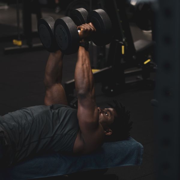 Person performing a dumbbell exercise on a bench, photo by Marius Aholou on Pexels