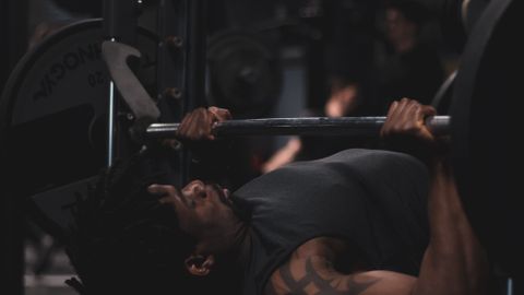 Man performing bench press in a dimly lit gym, focused on weight training.