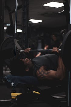 Man performing bench press in a dimly lit gym, focused on weight training.