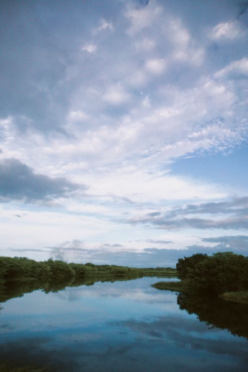 Free Calm river reflecting a cloudy sky, surrounded by lush greenery. Stock Photo