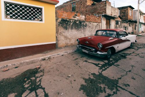Free Classic vintage car parked on a rustic street with aged buildings in the background. Stock Photo