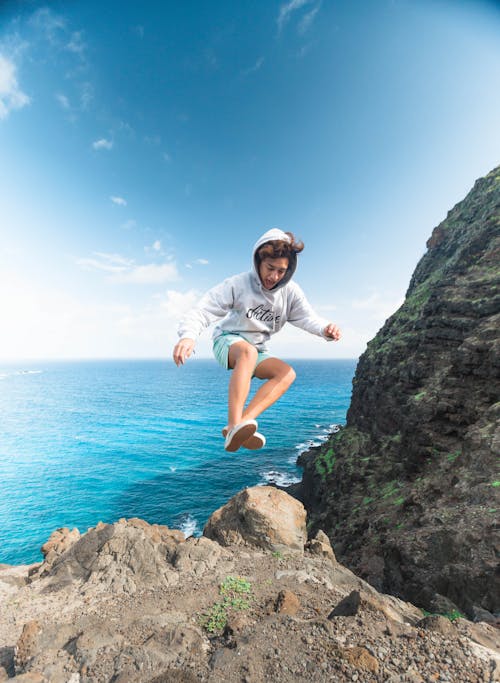 Free Man Wearing Gray Hoodie Jumping at Rock Stock Photo