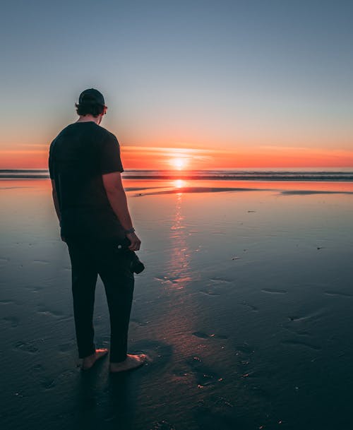 在日落时站在海滩上的男人