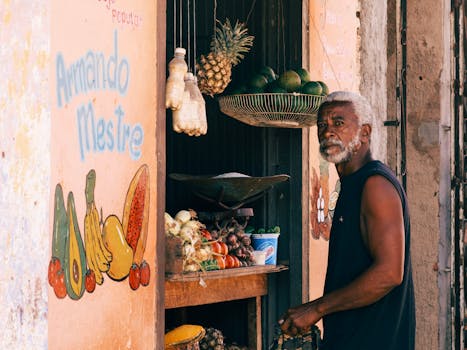 Elderly vendor with white hair at a rustic fruit market stand selling fresh produce.