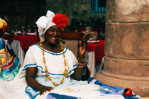 Free African woman in traditional dress smiling and smoking a cigar outdoors. Stock Photo