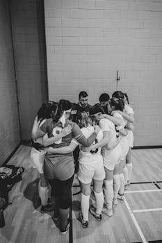Women's soccer team huddling indoors, creating a strong team unity atmosphere in monochrome.