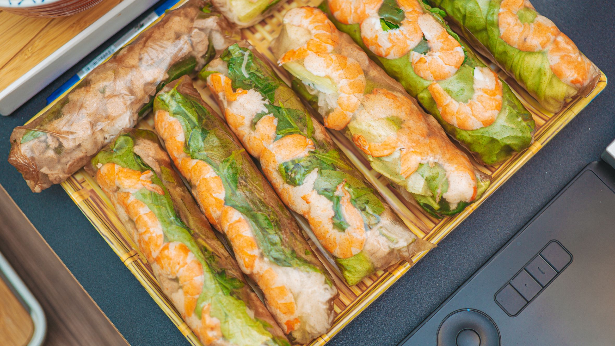 Close-up of fresh Vietnamese spring rolls filled with shrimp, lettuce, and rice noodles on a bamboo tray.