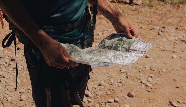 A hiker studies a map on a sunny day, exploring a rugged outdoor trail.