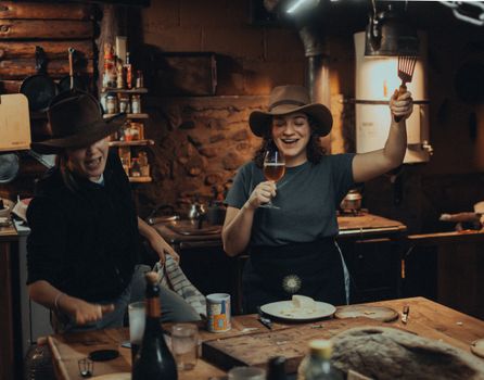 Friends having fun and cooking together, enjoying drinks in a cozy rustic kitchen.